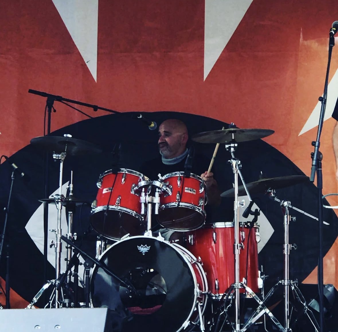 Johnny Torres playing a red drum kit on stage, captured mid-performance with microphones and cymbals around him.