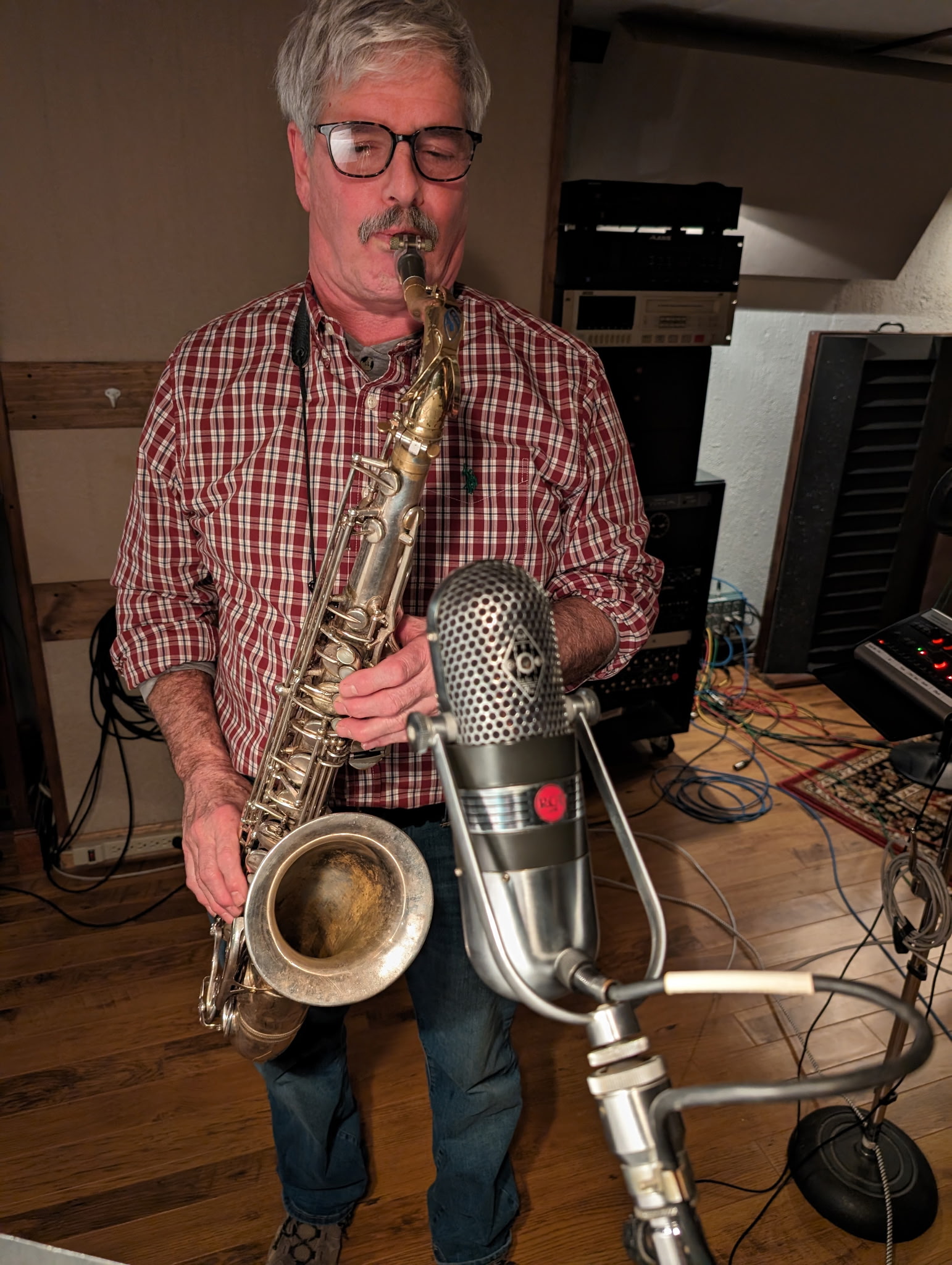 A saxophonist records a live take in the studio, leaning into the mic as the room fills with tone.